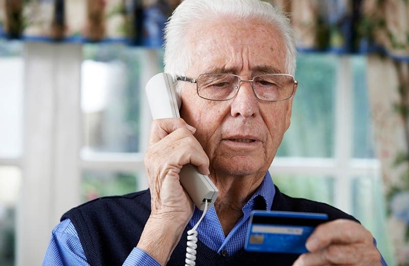 older man holding credit card and talking on phone
