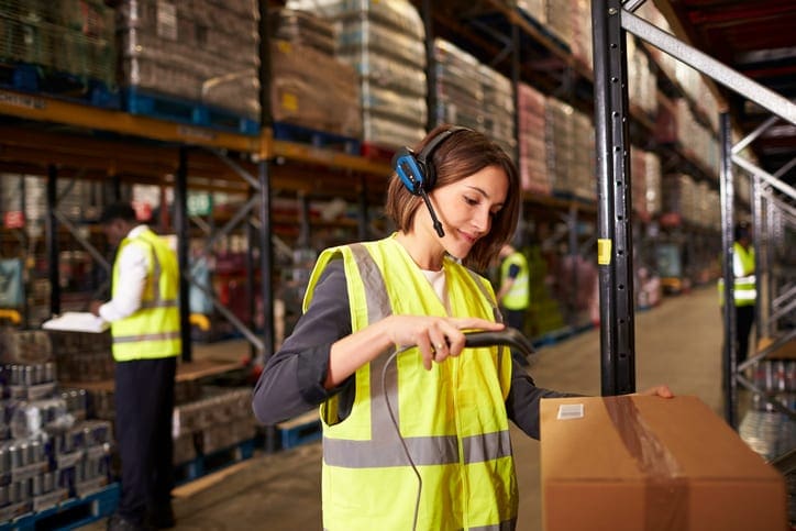 woman working in warehouse wearing yellow safety vest scanning inventory