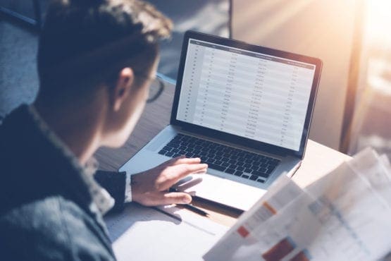 professional male looking at laptop screen holding financial papers