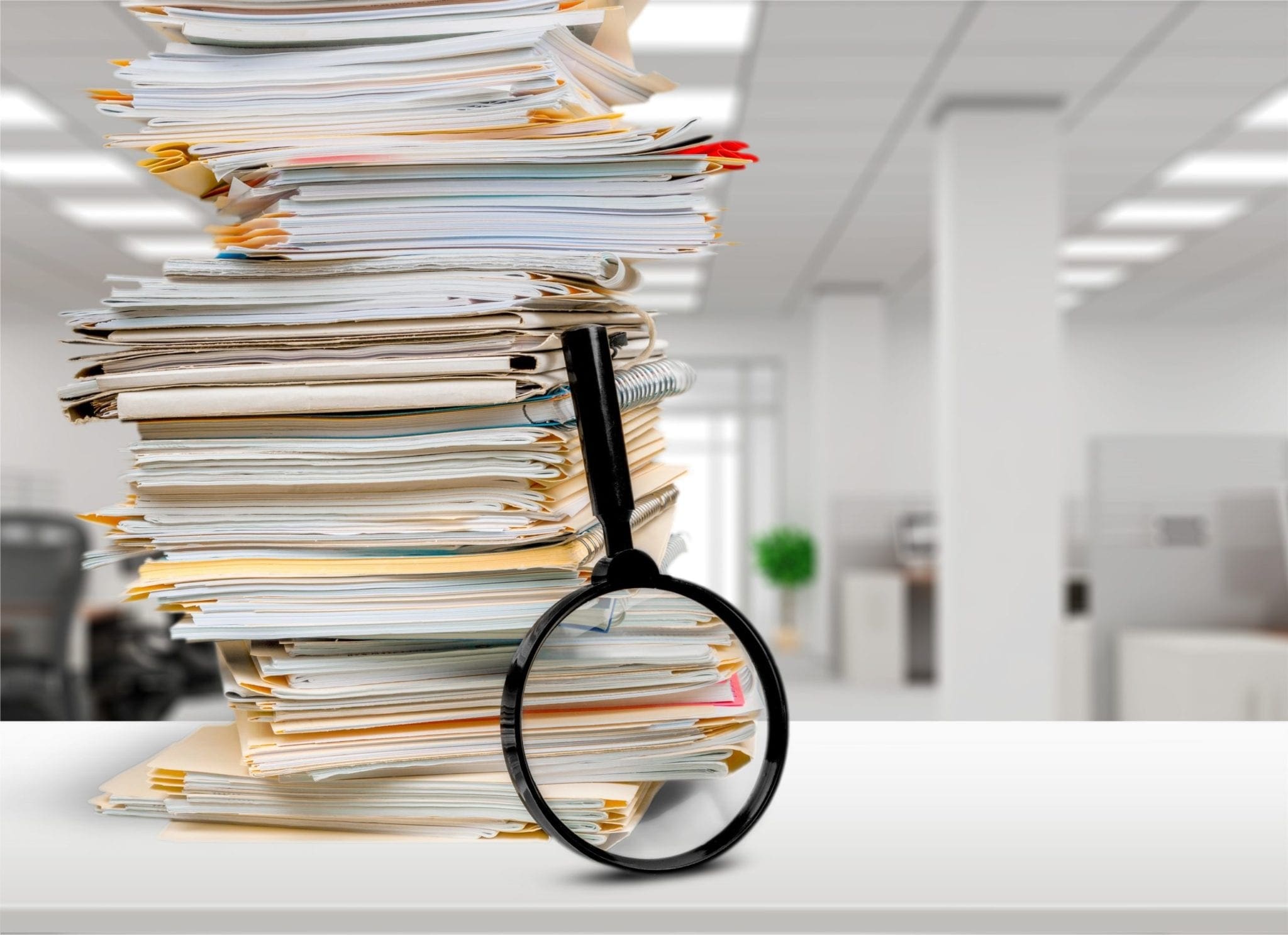 large stack of papers with magnifying glass