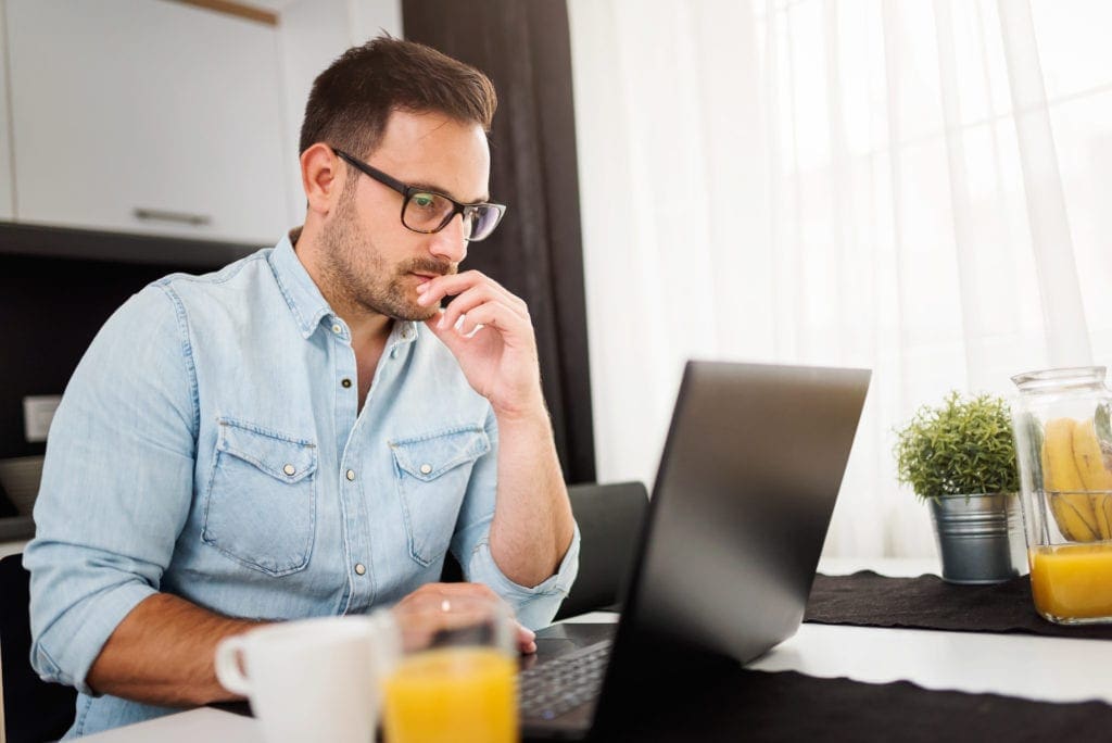 Man using laptop computer, working at home. Worried about finances, used byAvidXchange for article summarizing new research regarding companies' ability to work from home and continue paying bills during the COVID-19 pandemic.