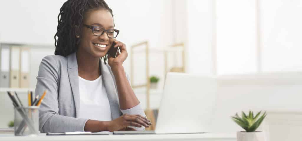 Black Businesswoman Talking on Cellphone and Using Laptop in Office.
