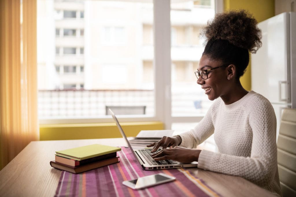 Woman smiling sitting in her apartment working on a laptop.