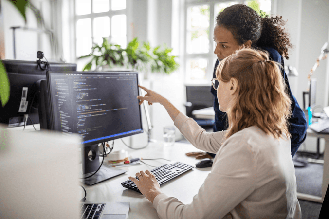 Two women working on a desktop computer looking at data on a monitor.