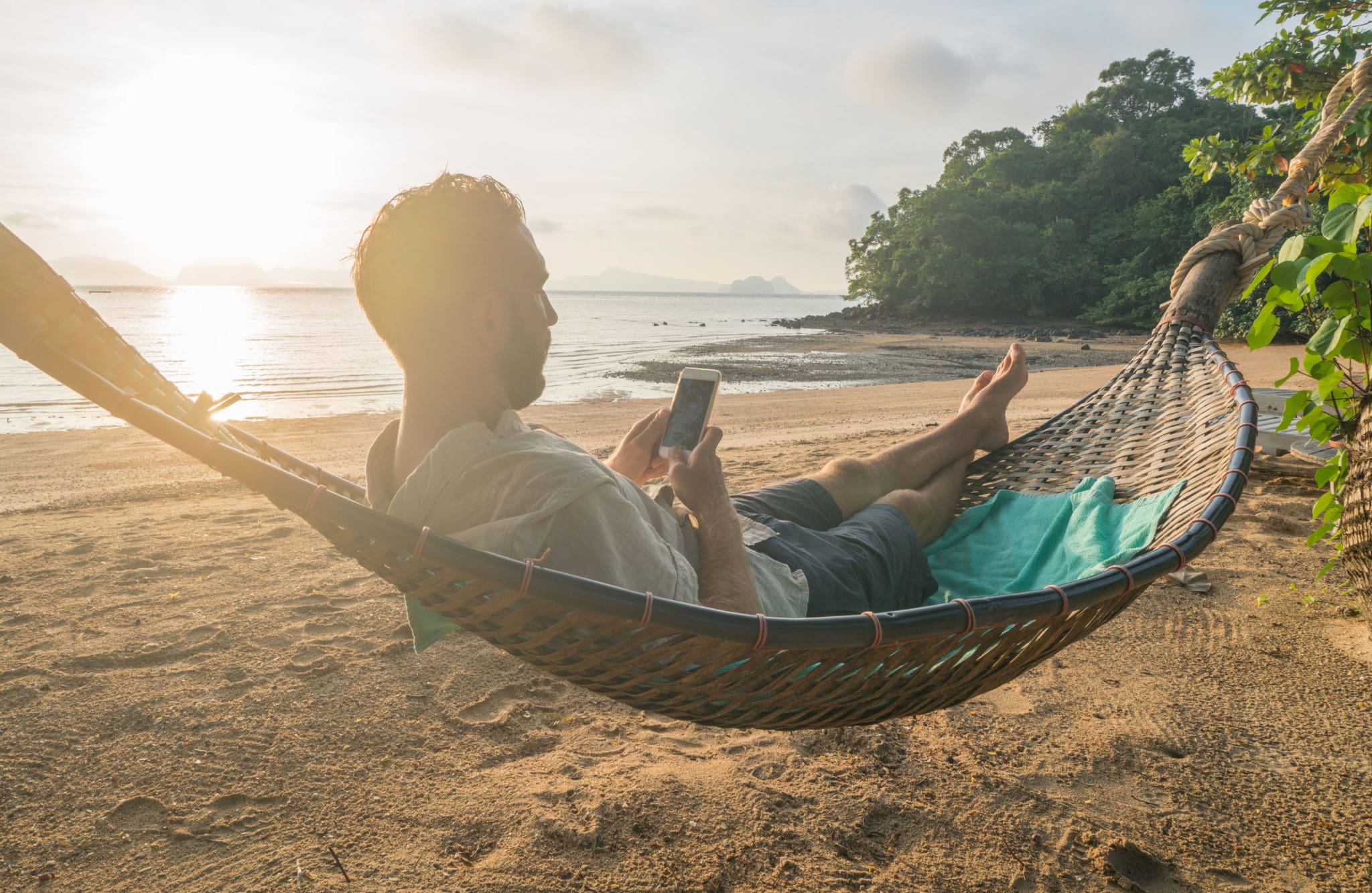 Man lays in hammock and uses smartphone