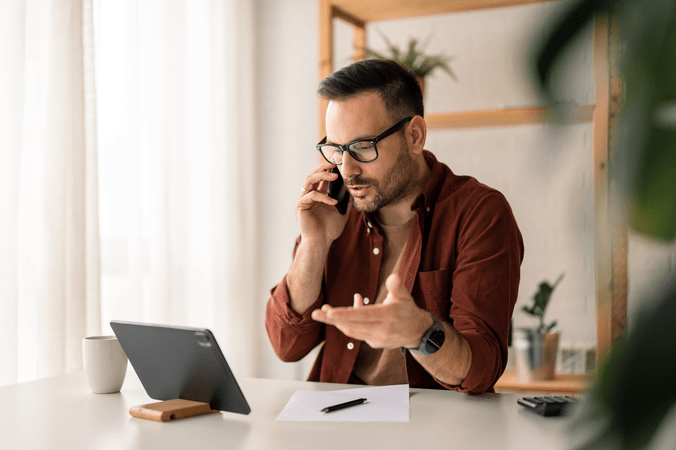 man on phone in front of laptop on desk