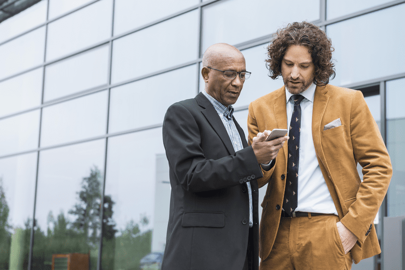 Two men looking at a phone outside of an office building.