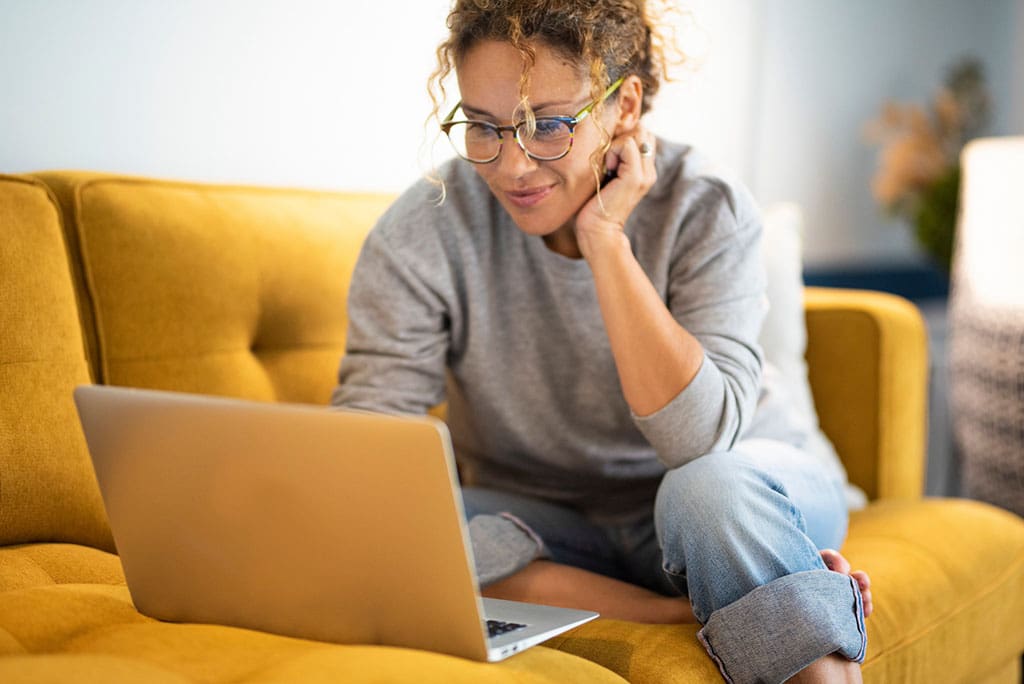 Female sitting on a yellow couch using laptop