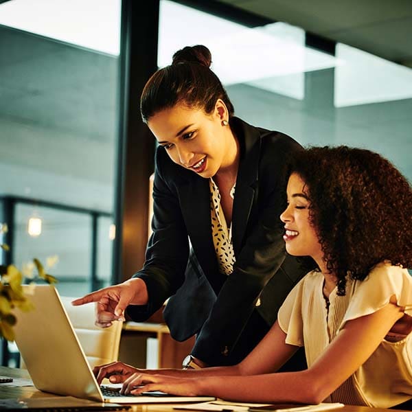 Two female co-workers smiling looking at a laptop.