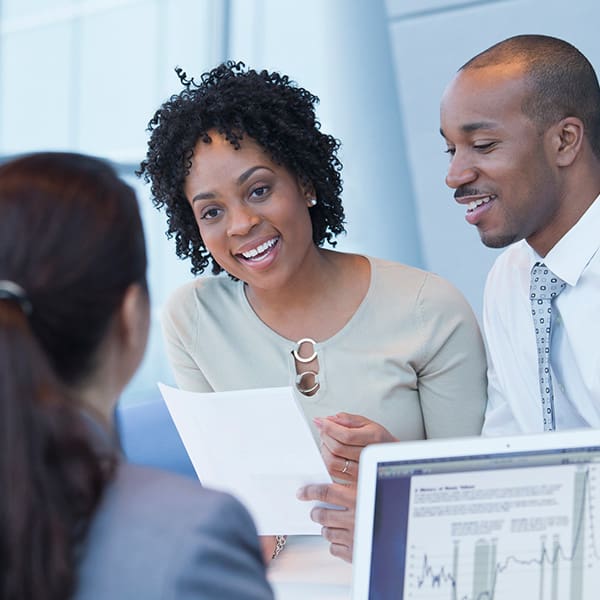 A young couple smiling and speaking with a bank manager.