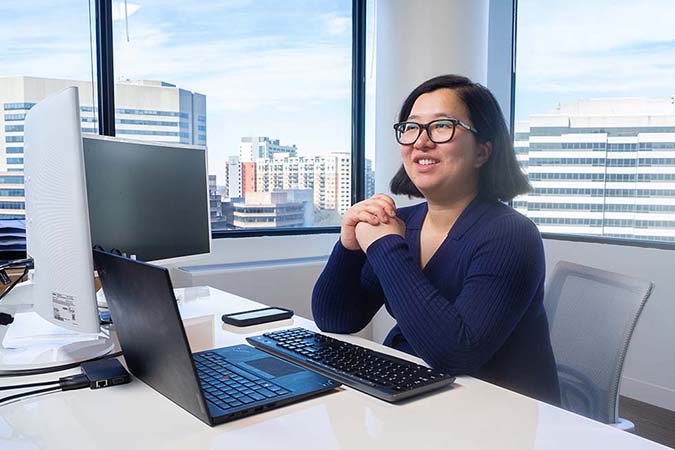 Ella Hu sitting at her desk smiling.