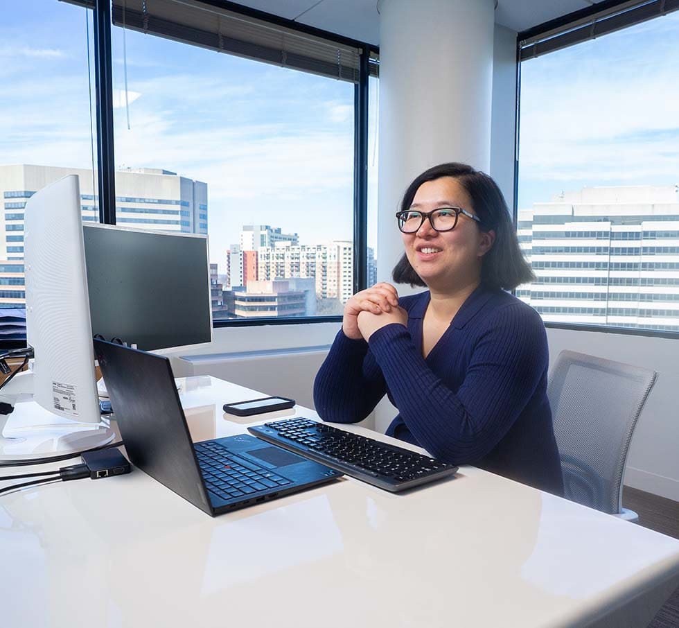 Ella Hu sitting at her desk smiling.
