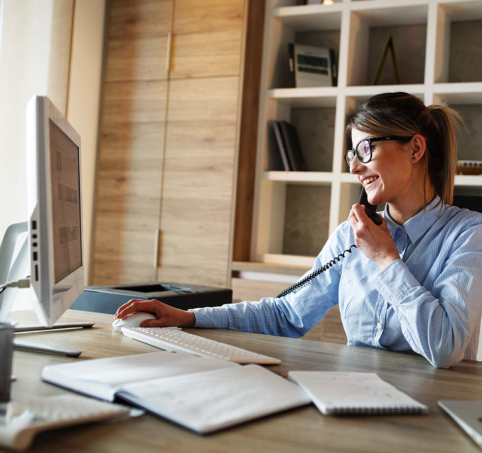 Woman on the phone smiling while working at her desk.