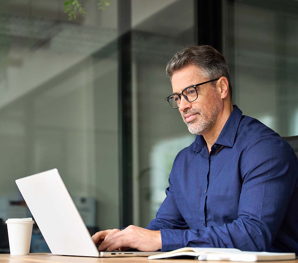 Finance executive wearing glasses, working on his laptop and smiling.