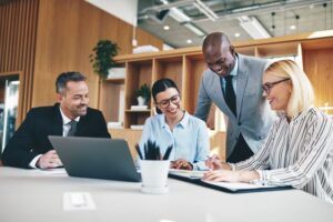 Diverse group of real estate businesspeople laughing while having a meeting about AP automation together around a table in an office