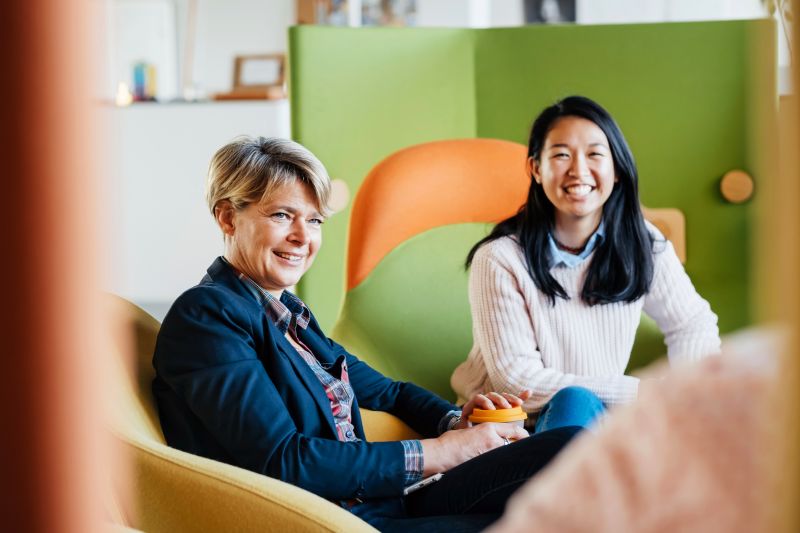 A business owner sitting down in a colorful chair alongside some colleagues during a meeting with some of her heads of staff.
