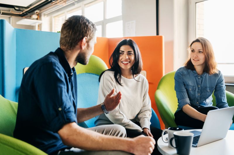 A meeting between three team leaders sitting in colorful chairs in a modern office environment.