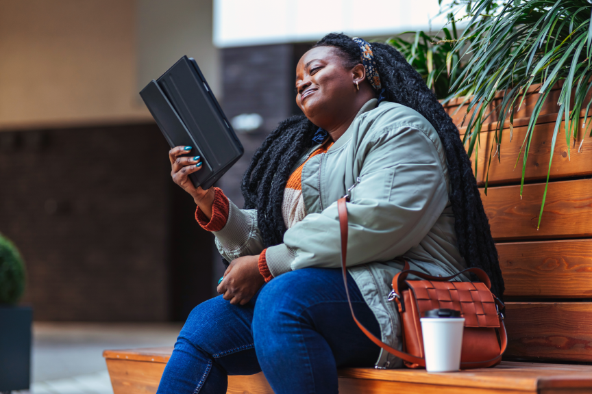Beautiful young african american woman making break, sitting on the bench and using digital tablet