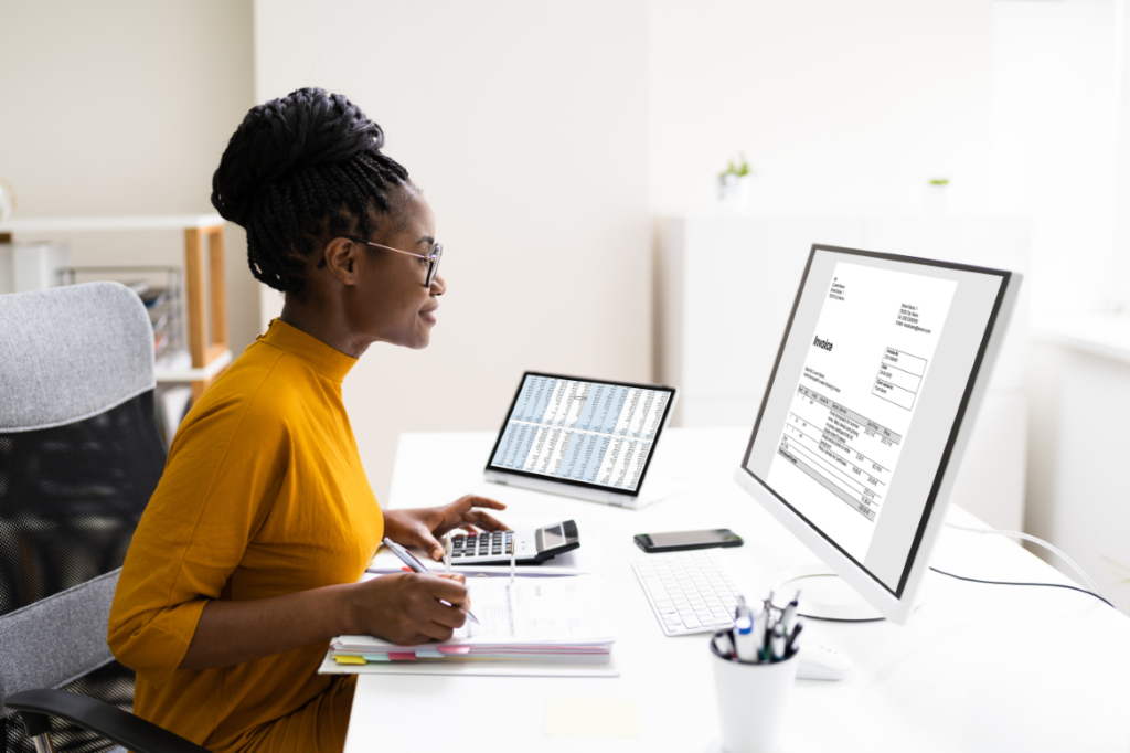 Woman working on finance tasks utilizing tech stack on the computer alongside a tablet and calculator