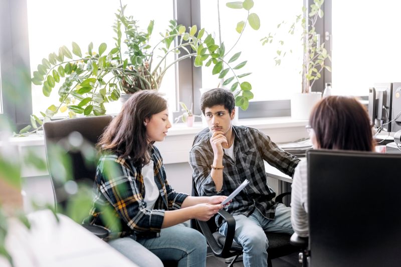 Group of people sitting in office having meeting. Woman holding a document and discussing with colleagues in office.